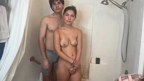 A video of a young, nude couple standing in a shower. The woman, with medium-sized breasts, stands facing the camera, while the man, wearing only blue boxer briefs, stands behind her.