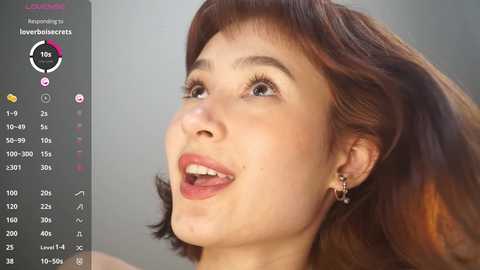Video of a smiling, light-skinned woman with short brown hair, wearing small earrings, against a blurred background.