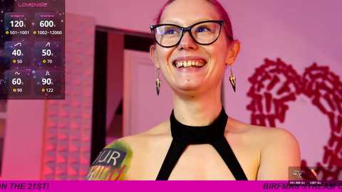 Video of a smiling, fair-skinned woman with glasses, wearing a black halter top, in a brightly lit room with a red lion mural.