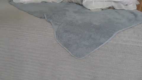 A close-up video of a light gray, textured blanket and a soft, light blue throw blanket neatly folded on a light beige, woven fabric surface.