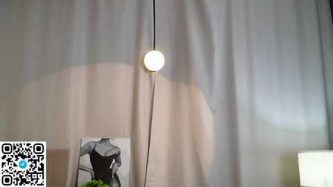 A video of a minimalist room with a large, sheer white curtain, a spherical white light, and a black-and-white portrait of a woman in a dress on a wall.