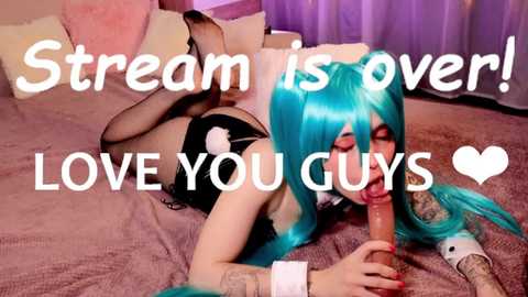 Video of a young woman with vibrant turquoise hair, wearing a black bunny costume, performing oral sex on a man's erect penis. She lies on a bed with pink and beige pillows. Text overlays read, \"Stream is Over! LOVE YOU GUYS.\