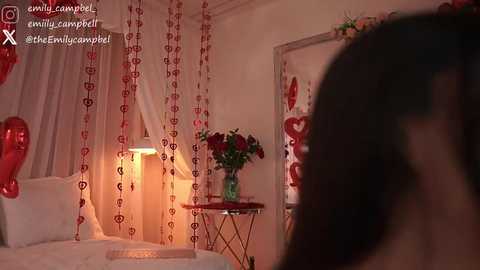 Video of a cozy bedroom with red heart curtains, heart-shaped pillows, and a small round table with a vase of red roses. Warm, romantic ambiance.