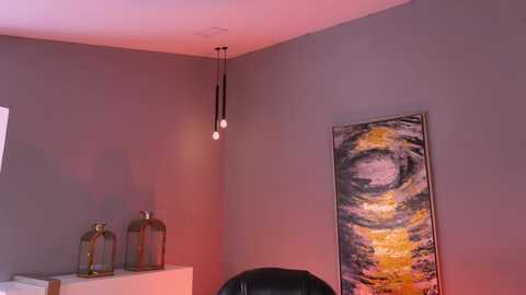 Video of a minimalist room corner with a grey wall, modern pendant lights, a black chair, and a vibrant abstract painting.