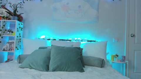 A serene, pastel-themed bedroom with white walls, a bed covered in white sheets, two teal pillows, and soft blue LED strip lighting under a white headboard. A small white shelf on the left holds a vase with flowers, and a closed door is visible on the right.