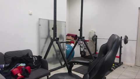 Video of a minimalist gym room with a black adjustable bench, blue dumbbells, a glass mirror, and a black leather chair.