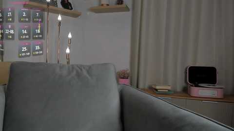 Video of a modern living room featuring a light gray sofa with a plush texture, wooden shelves with a retro clock, and a pink radio on a wooden cabinet.